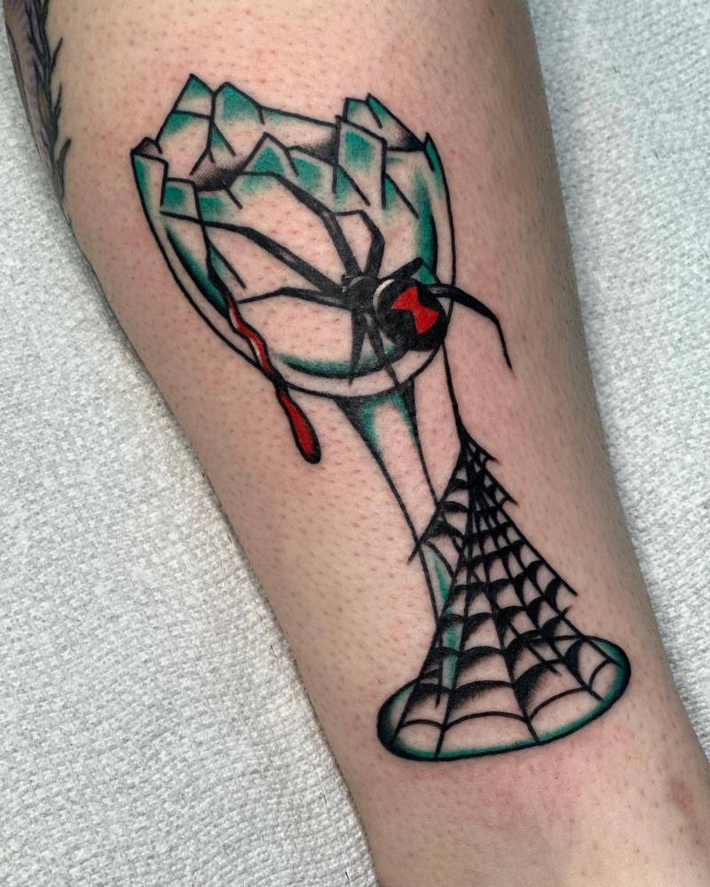 Broken wine glass and spider tattoo located on the shin.