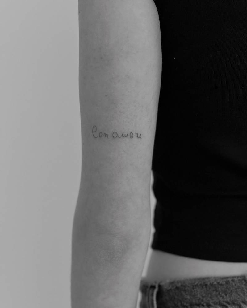 Handwritten font "con amore" lettering tattoo placed on the tricep.