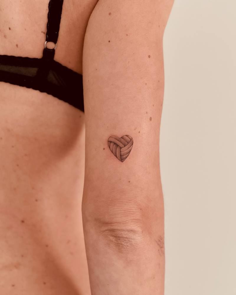 Volley ball heart tattooed on the tricep, illustrative style.