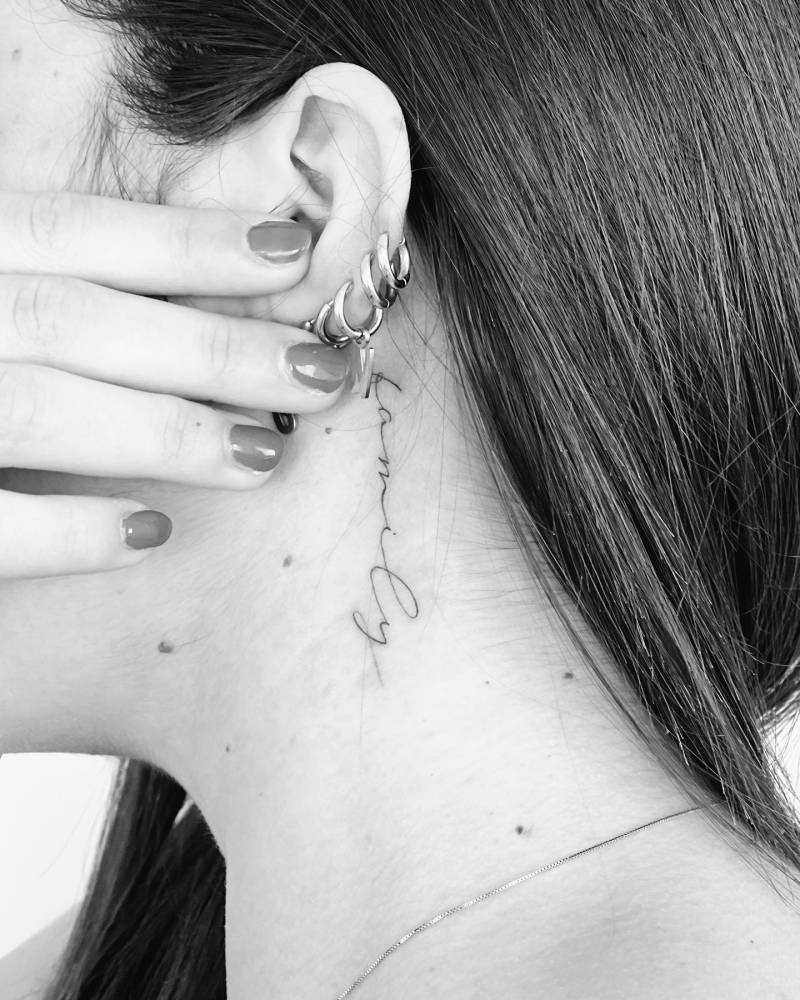 "Kamily" handwritten lettering tattoo located behind the ear.