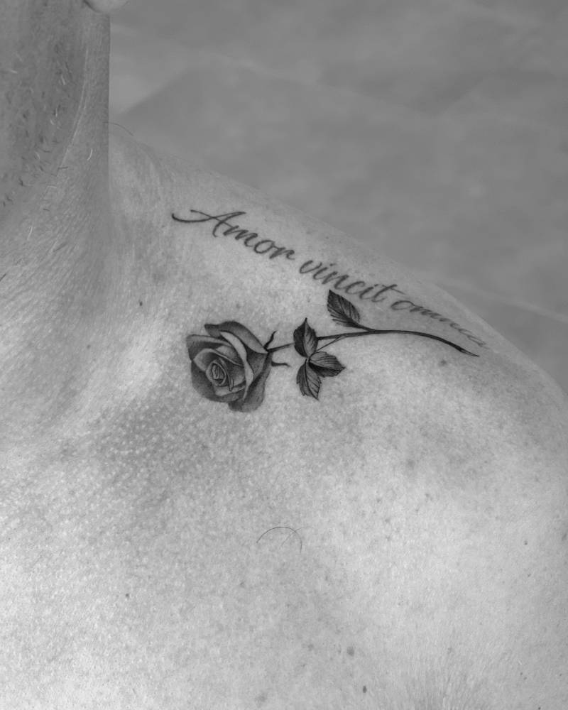 Rose and "amor vincit omnia" tattoo located on the top of shoulder.