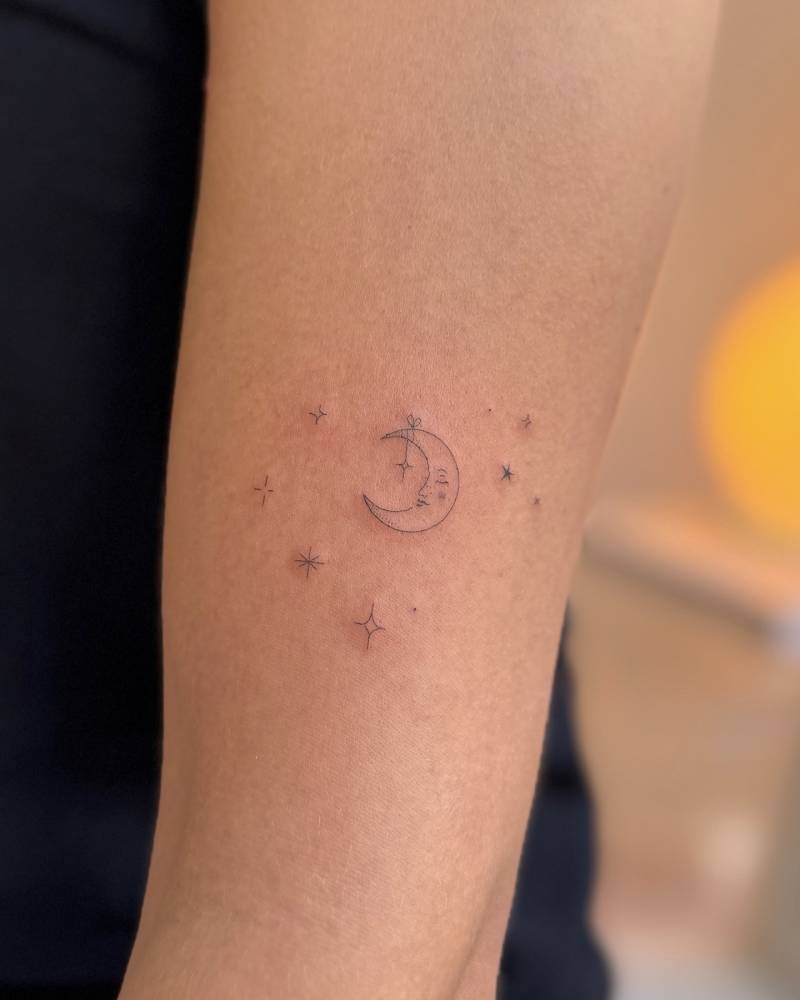 Moon face and stars tattoo located on the upper arm, fine line style.