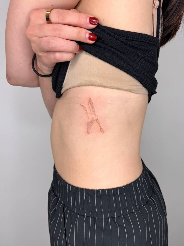 Crane tattoo in fine line style located on the rib.