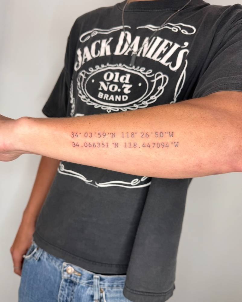 Typewriter font coordinates tattoo located on the forearm.