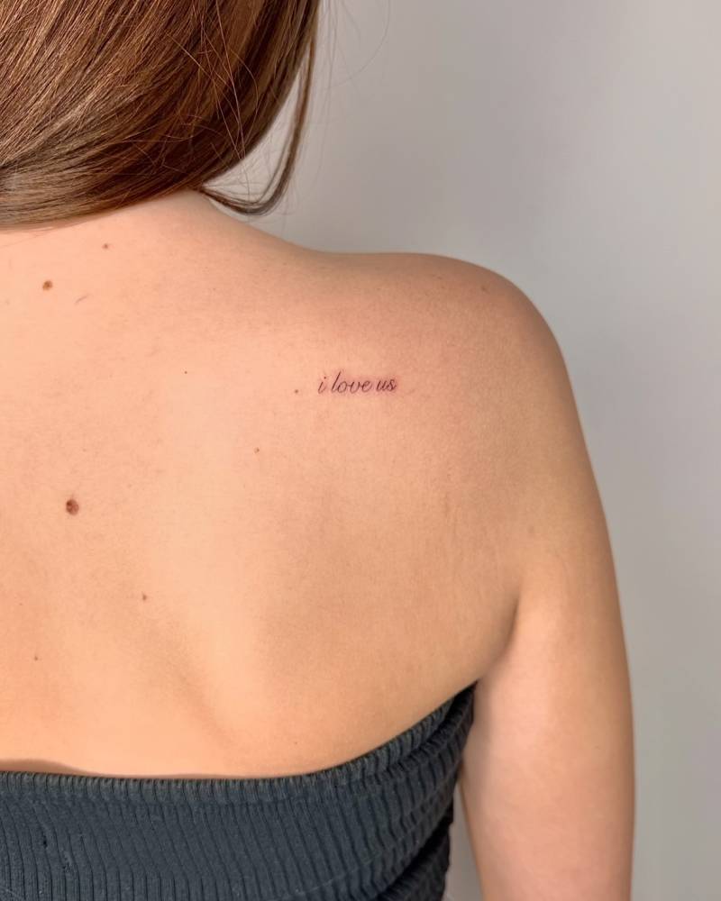 "I love us" lettering tattoo located on the shoulder blade.