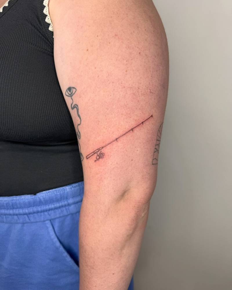 Little fishing rod tattoo in fine line style placed on the upper arm.