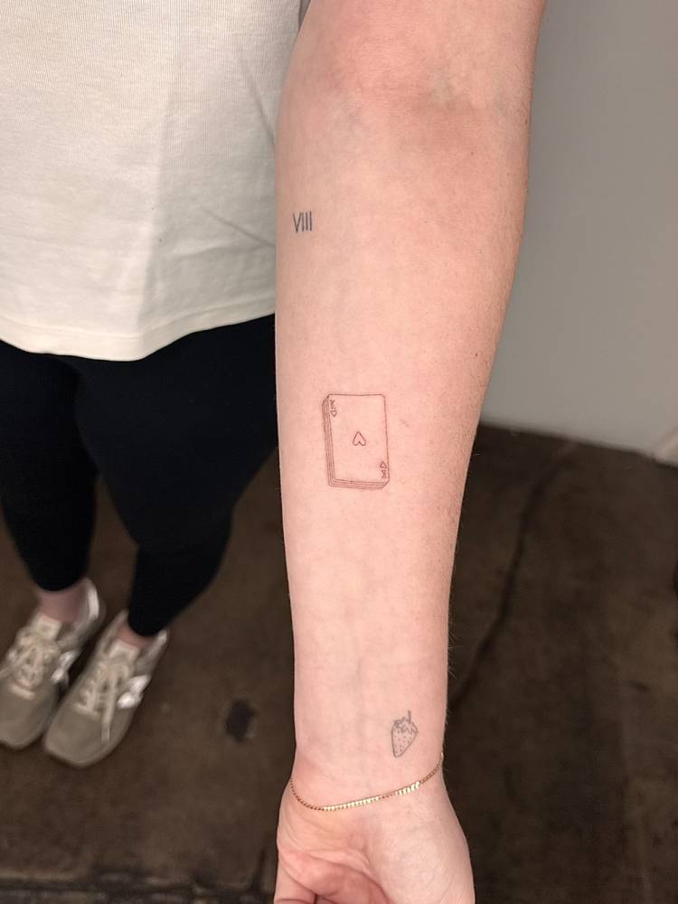 Ace of hearts tattoo in fine line style located on the inner forearm.