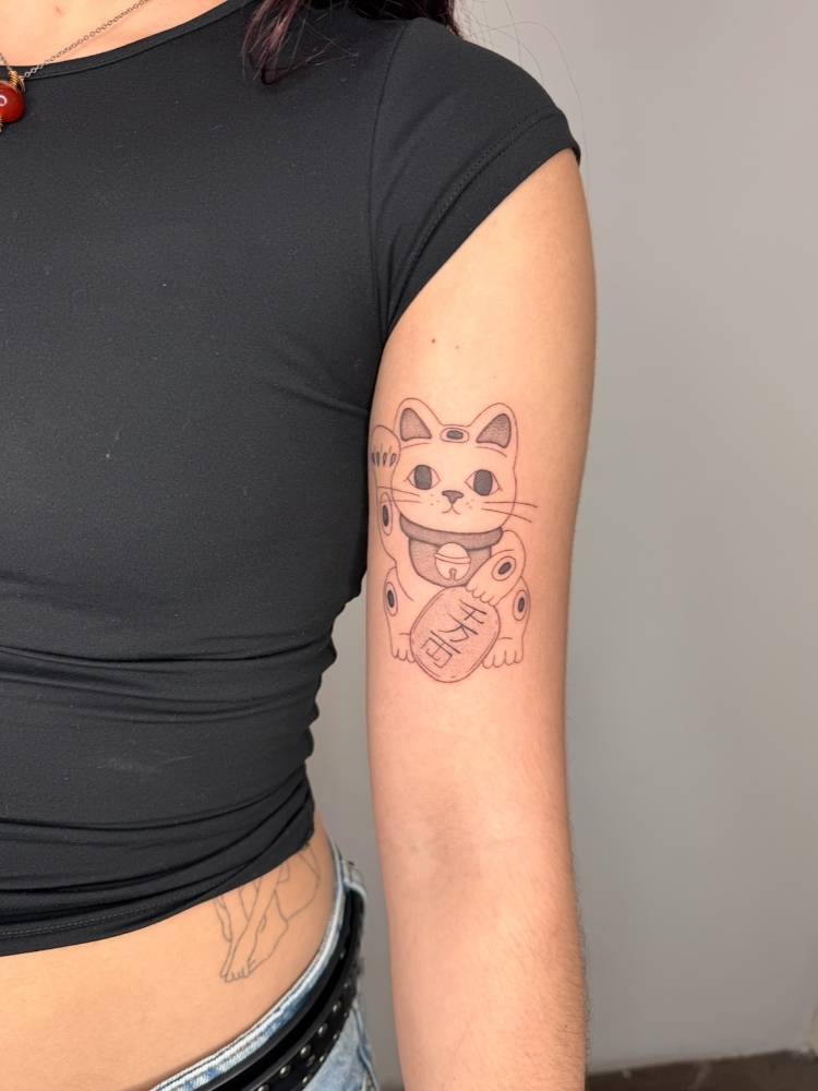 Single needle Maneki-Neko tattoo located on the bicep.