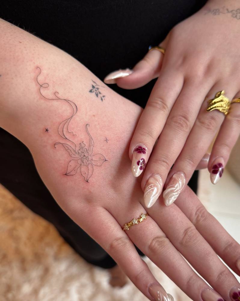 Orchid tattoo in fine line style located on the hand and wrist.