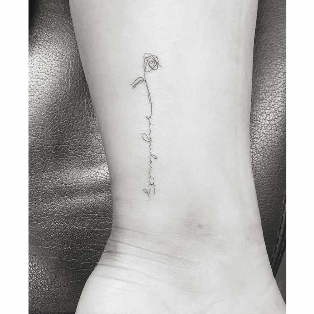 One line rose and word "singularity" tattoo placed on the ankle.