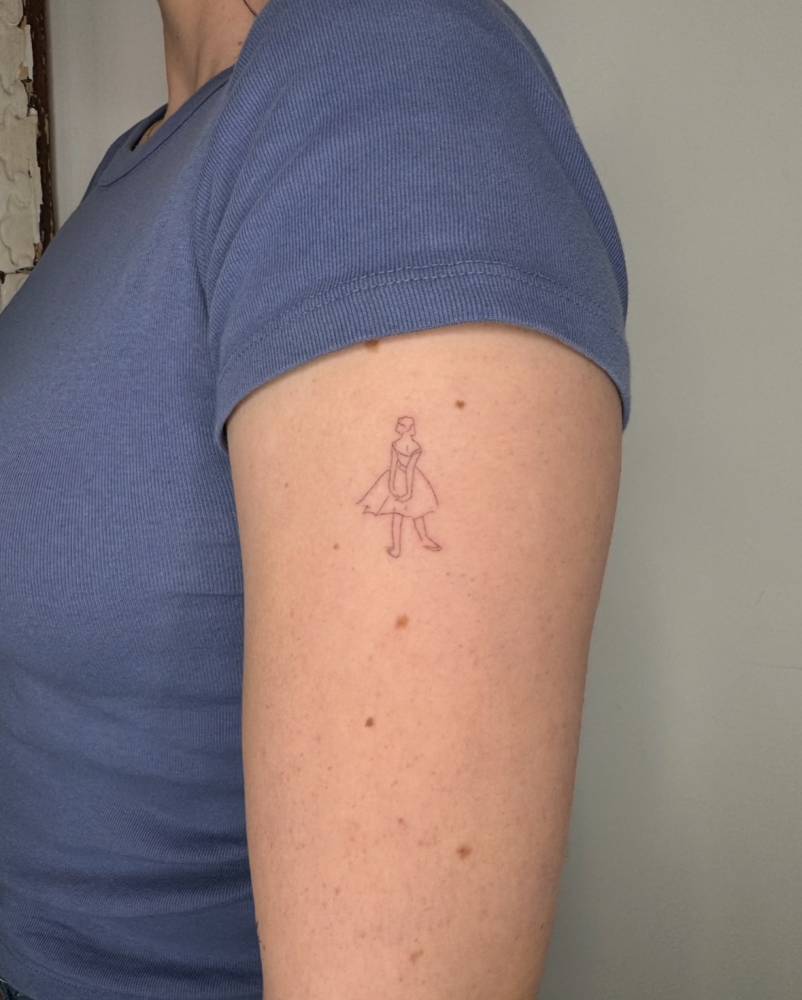 Little fine line style ballerina tattoo located on the upper arm.