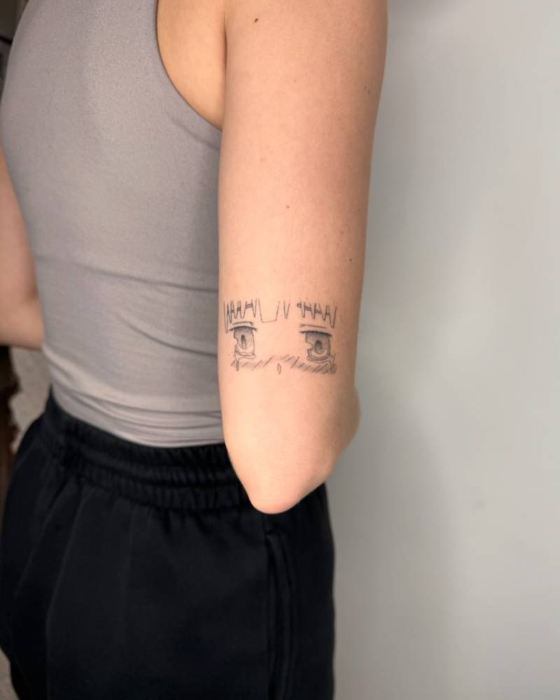 Cartoon style crying eyes tattoo located on the tricep.