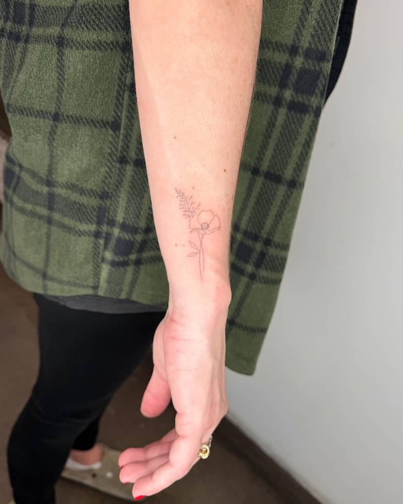 Fine line style poppy flower tattoo located on the wrist.