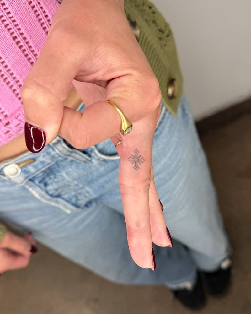 Fine line style little cross tattoo located on the finger.