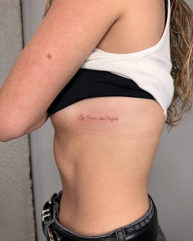 "Je t'aime pour toujour" handwritten lettering tattoo placed on the side boob.
