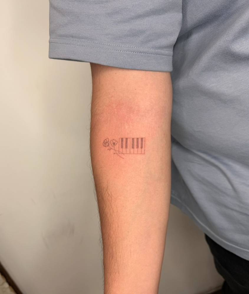 Single needle poppy flowers and piano keys tattooed on the inner forearm.