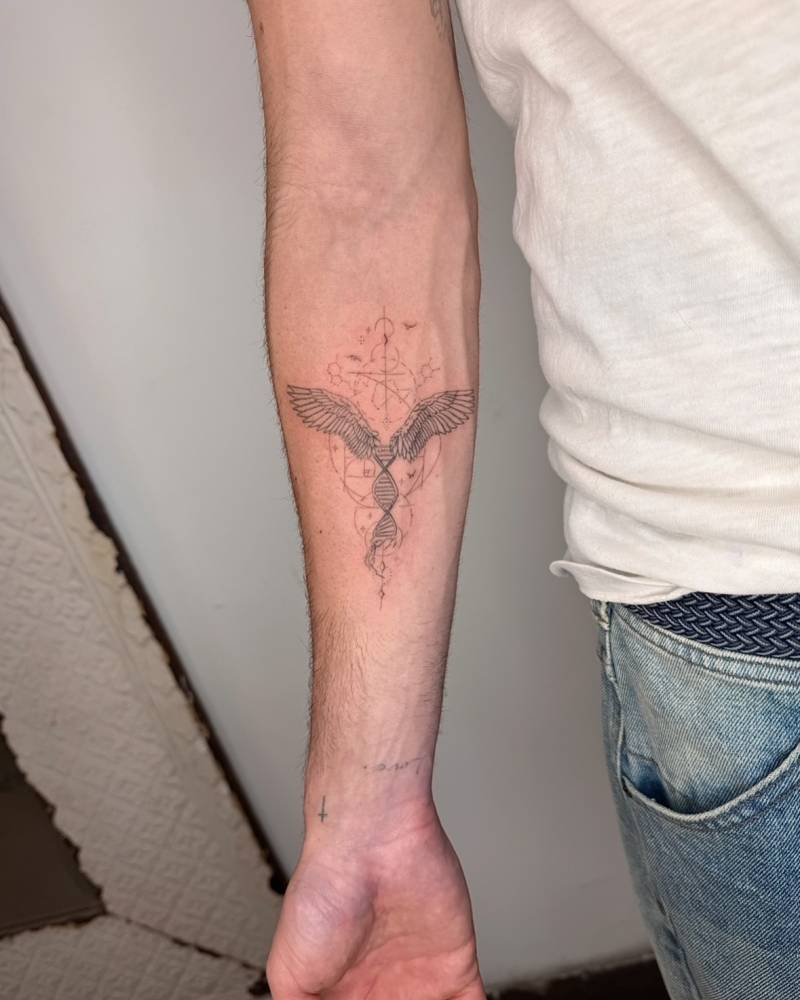 Graphic style DNA and angel wings tattoo located on the inner forearm.