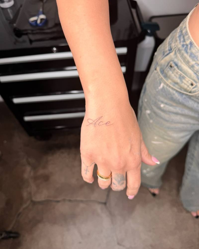 Handwritten lettering tattoo of the word "Ace" located on the hand.