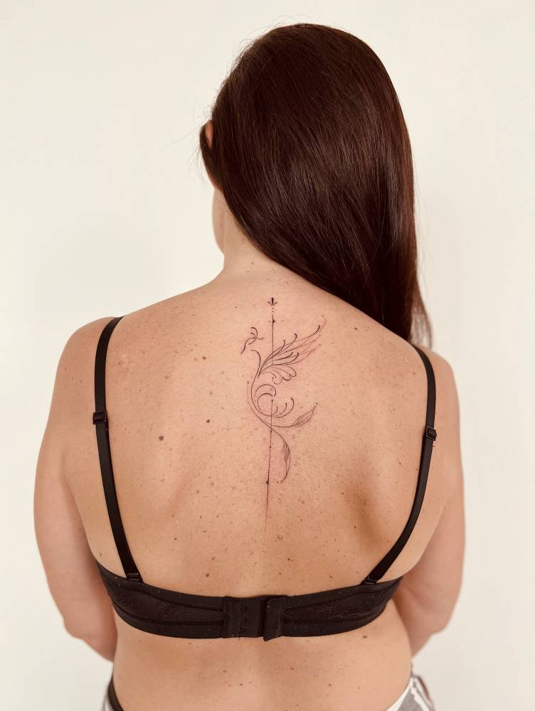 Phoenix tattoo located on the upper back, done in fine line style.