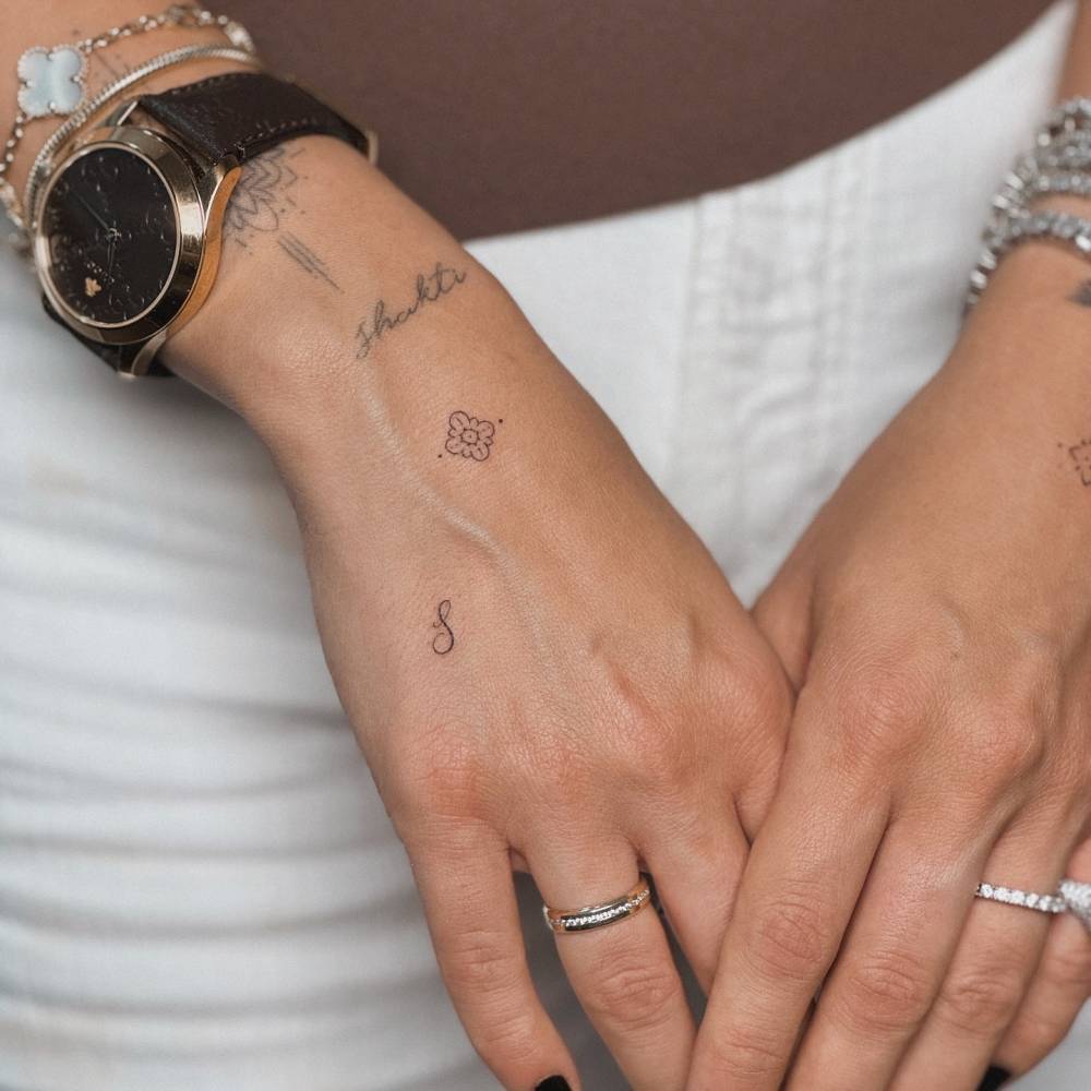 Tiny letter "S" and ornament tattoos located on the hand.