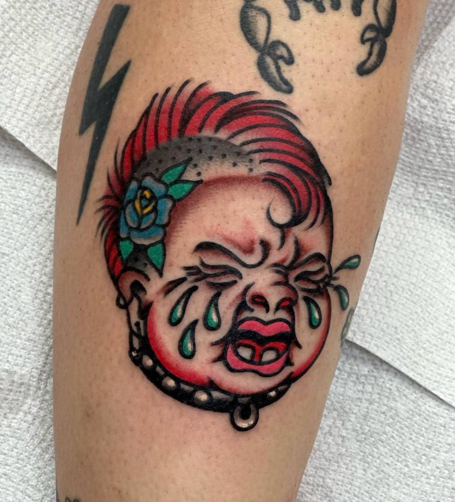 Crying punk baby tattooed on the shin, done in traditional style.