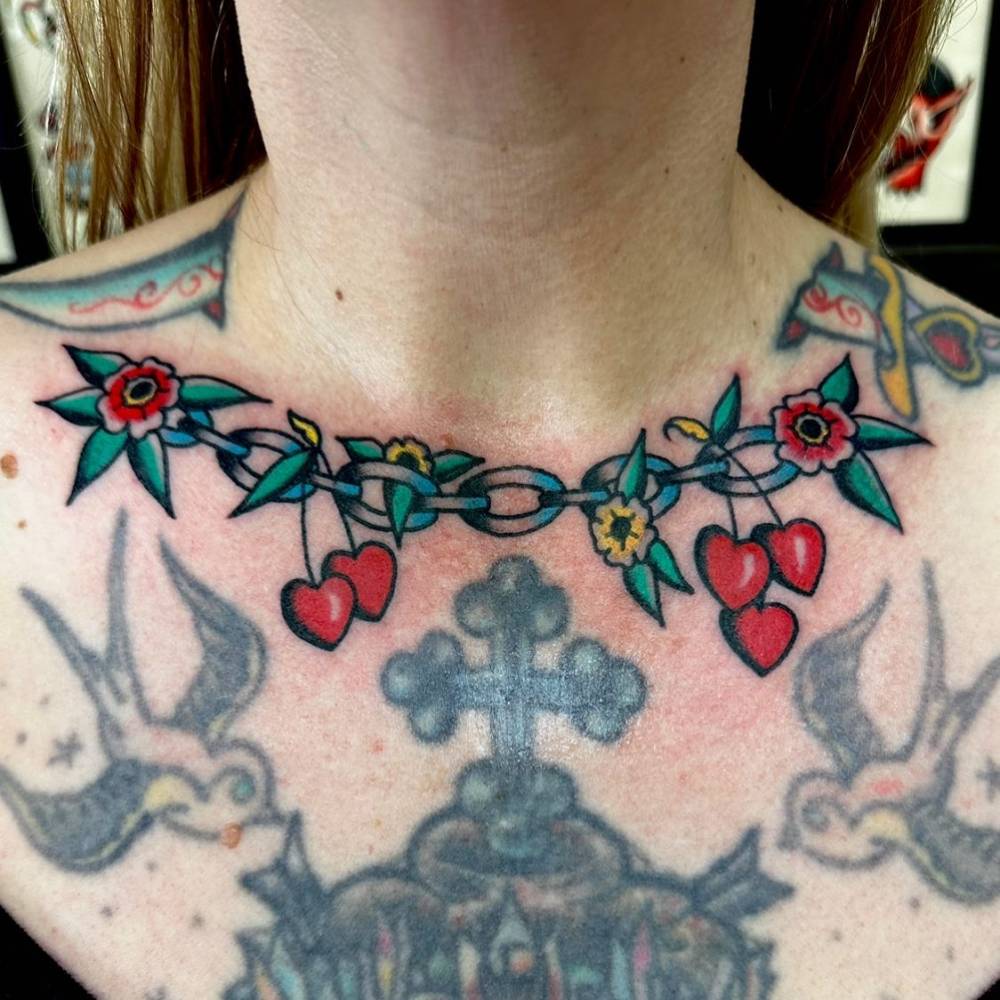 Chain, flowers and cherry hearts tattoo in traditional style placed on the collarbone.