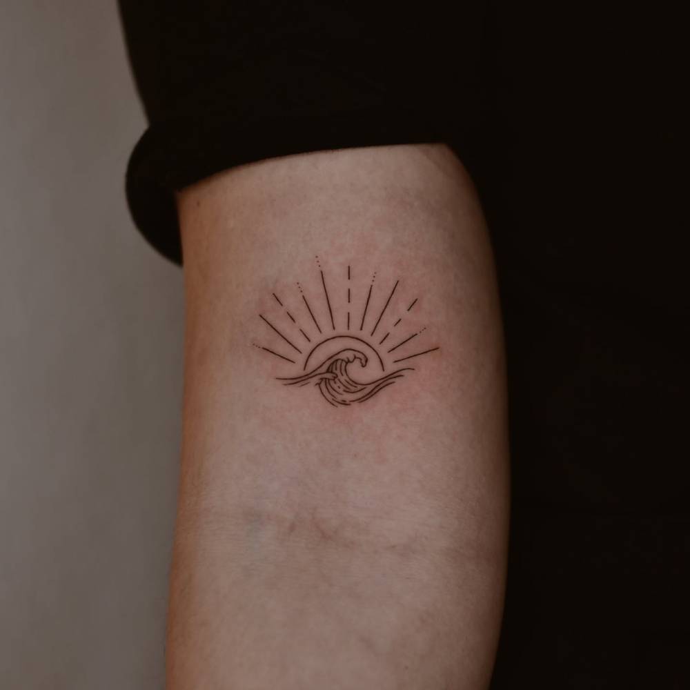 Little sun and wave tattoo located on the bicep.