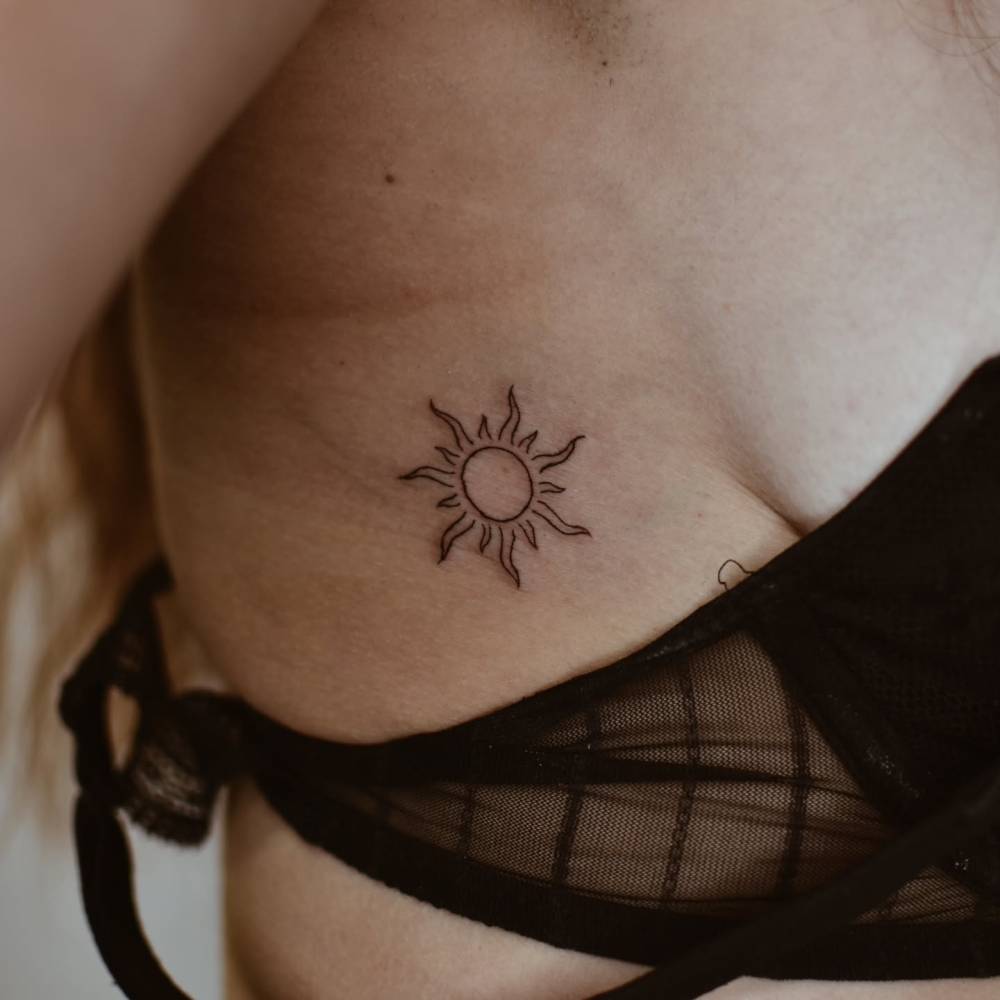 Line art style sun tattoo located on the side boob.
