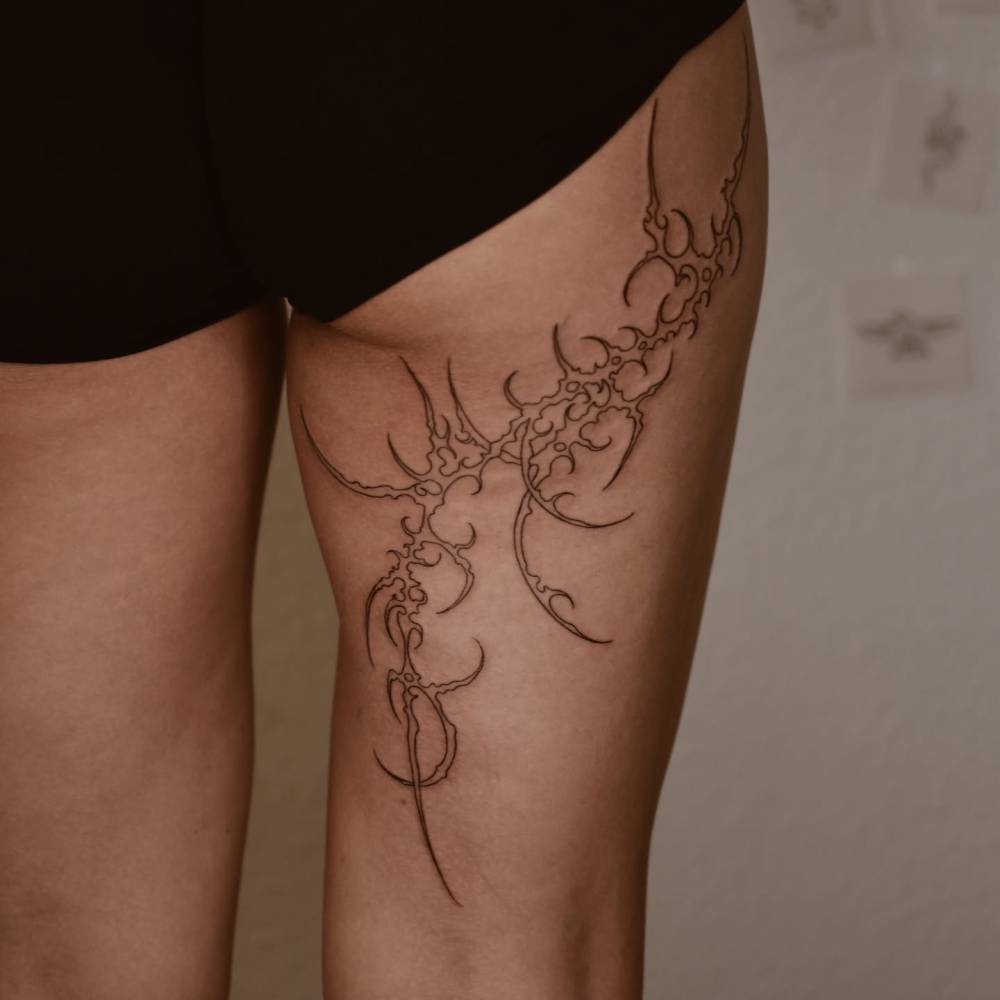Tribal design in fine line style tattooed on the thigh.