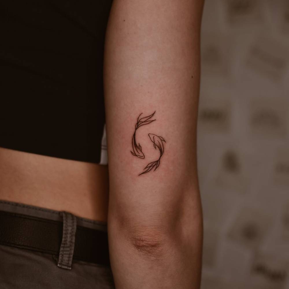Minimalistic style two opposite fish tattoo located on the tricep.