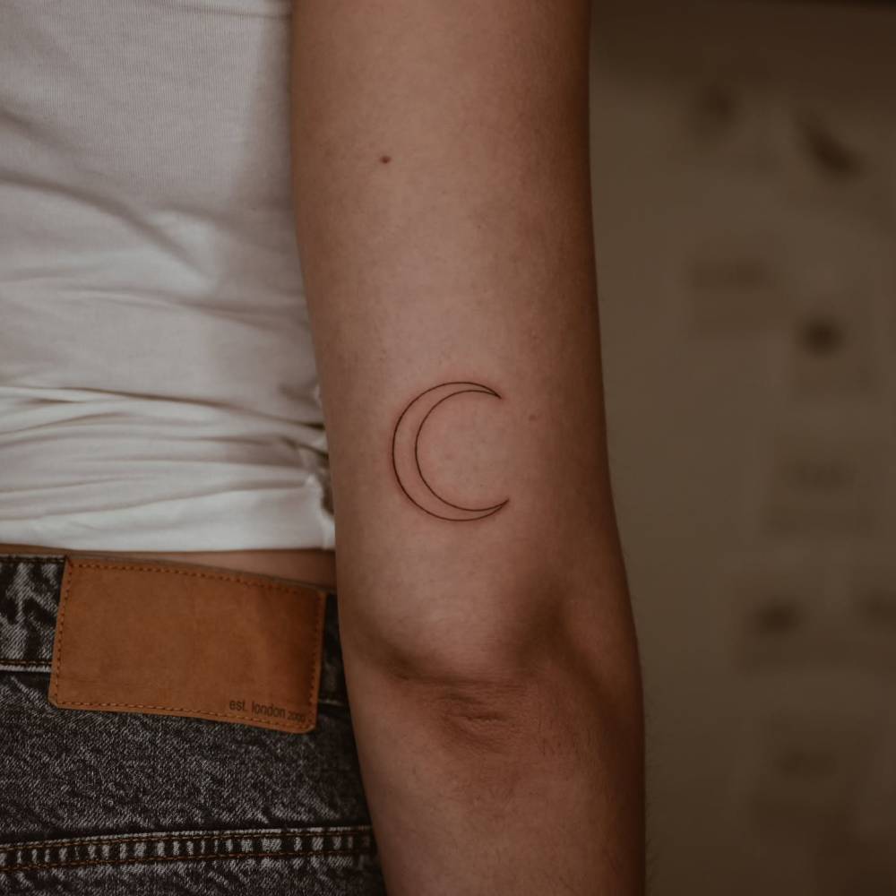 Crescent moon tattoo in fine line style placed on the tricep.