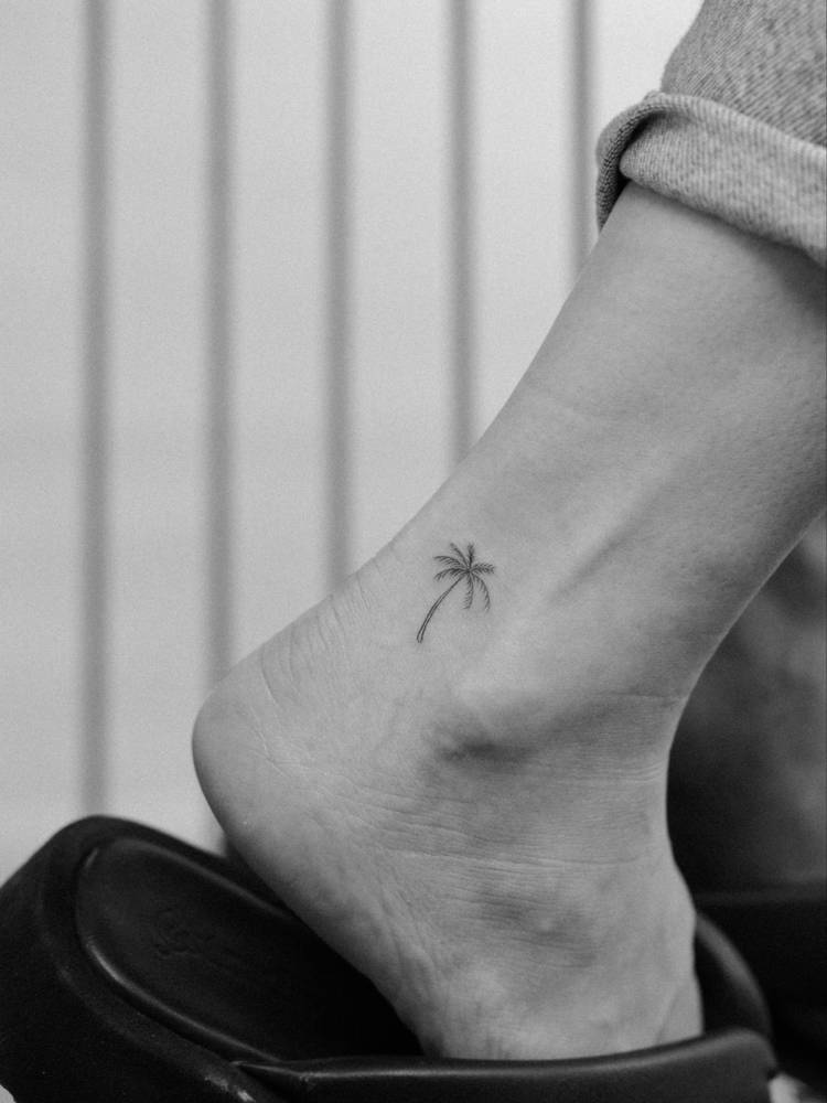 Little palm tree tattoo in fine line style placed on the ankle.