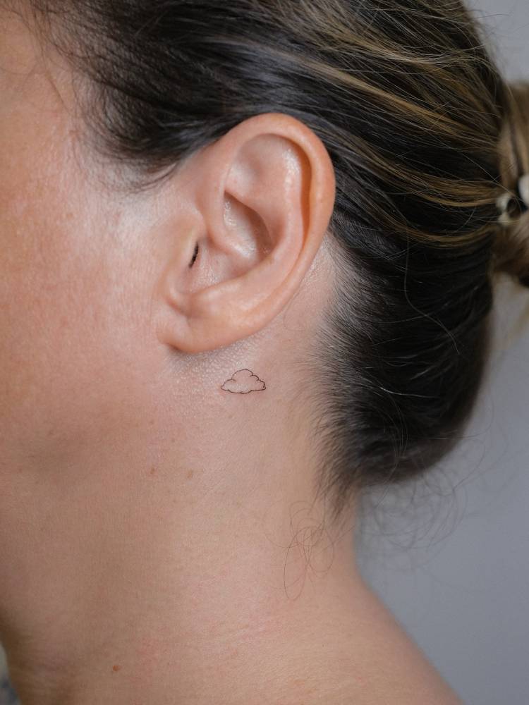Tiny minimalistic cloud tattoo placed behind the ear.