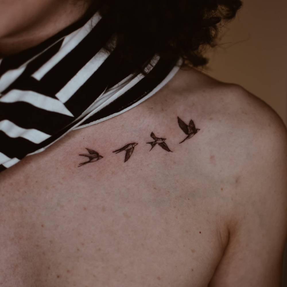 Flying swallows tattoo in illustrative style located on the collarbone.
