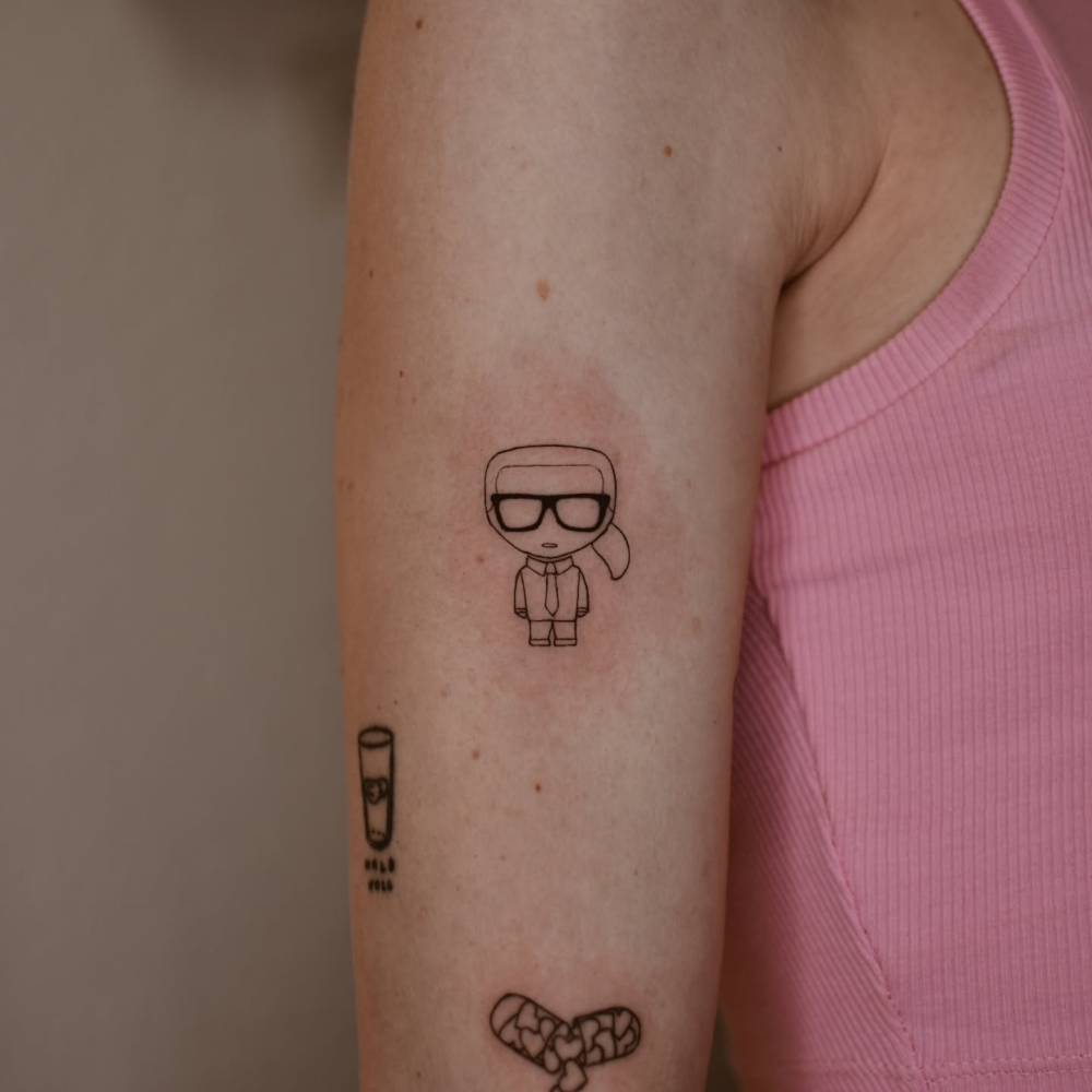 Karl Lagerfeld tattoo in cartoon style located on the upper arm.
