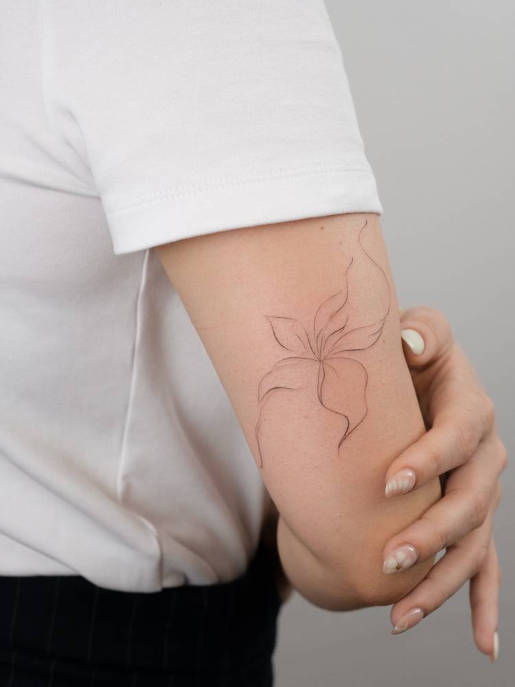 Lily flower tattoo in fine line style located on the tricep.