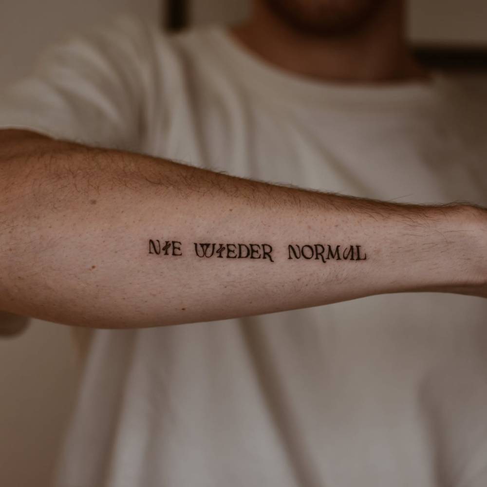 "Nie wieder normal" lettering tattoo located on the forearm.