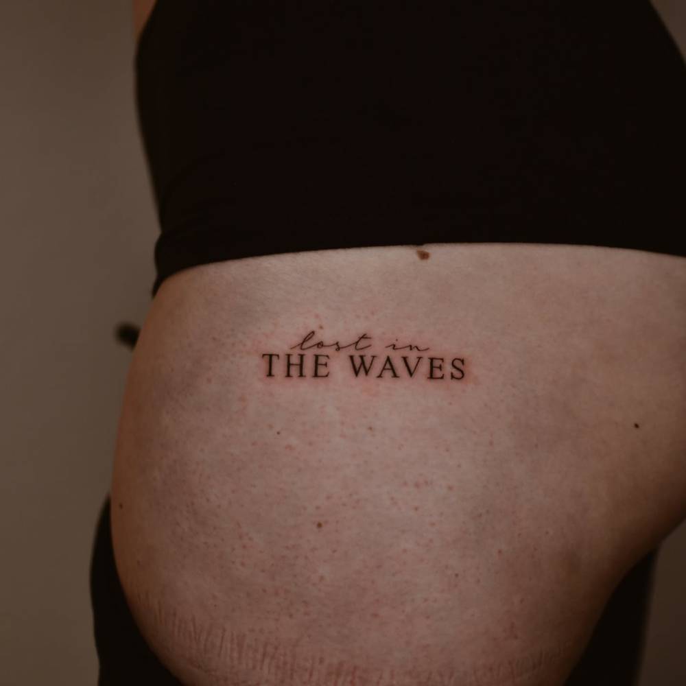 "Lost in the waves" lettering tattoo located on the hip.
