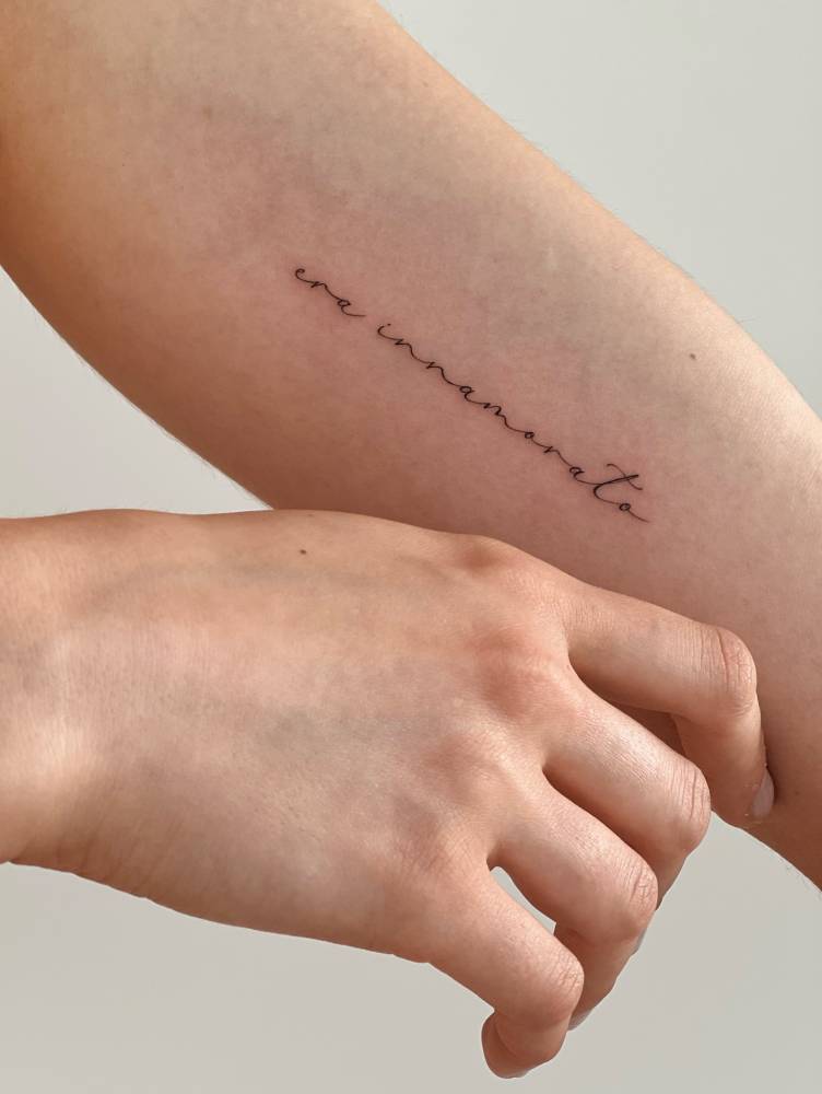 "Era innamorato" lettering tattoo located on the inner forearm.