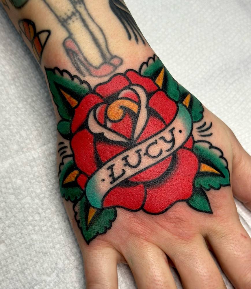 Red rose and banner with name "Lucy" tattooed on the hand.