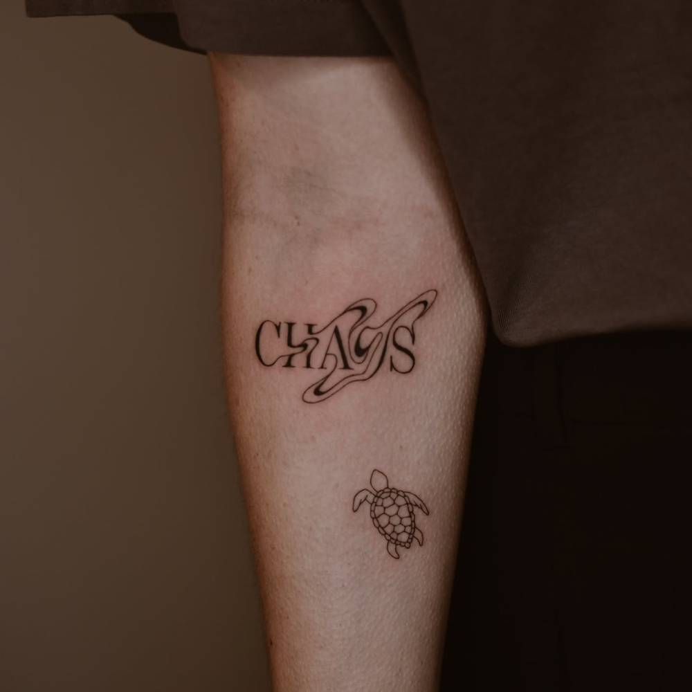 Abstract word "chaos" and little turtle tattooed on the inner forearm.