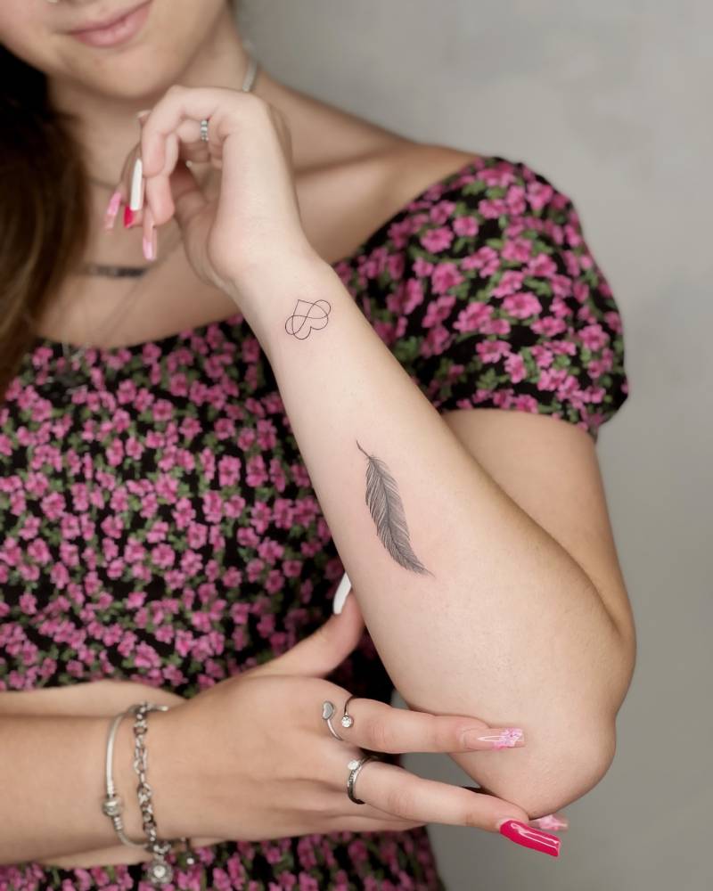 Infinity heart and feather tattoos located on the forearm.