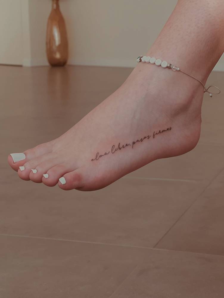 "Alma libre, pasos firmes" lettering tattoo handwritten on the foot.