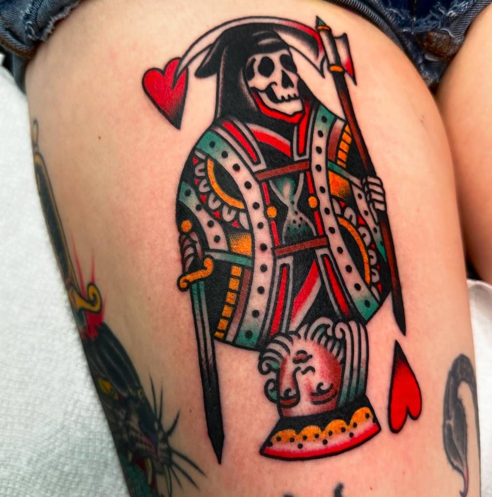 King of hearts and grim reaper tattoo located on the thigh, done in traditional style.