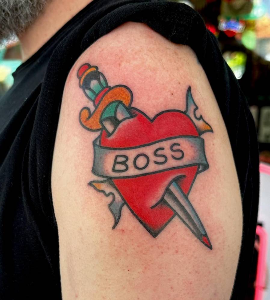 Heart and dagger with a "boss" banner tattooed on the upper arm.