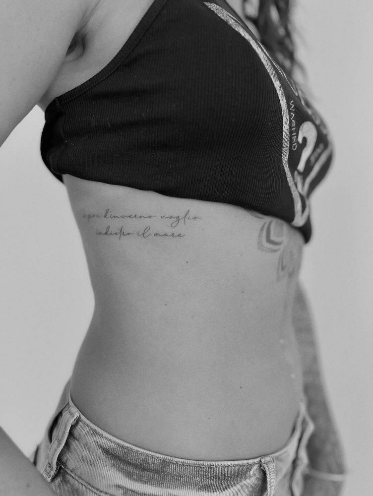 Italian quote in handwritten font tattooed on the rib.
