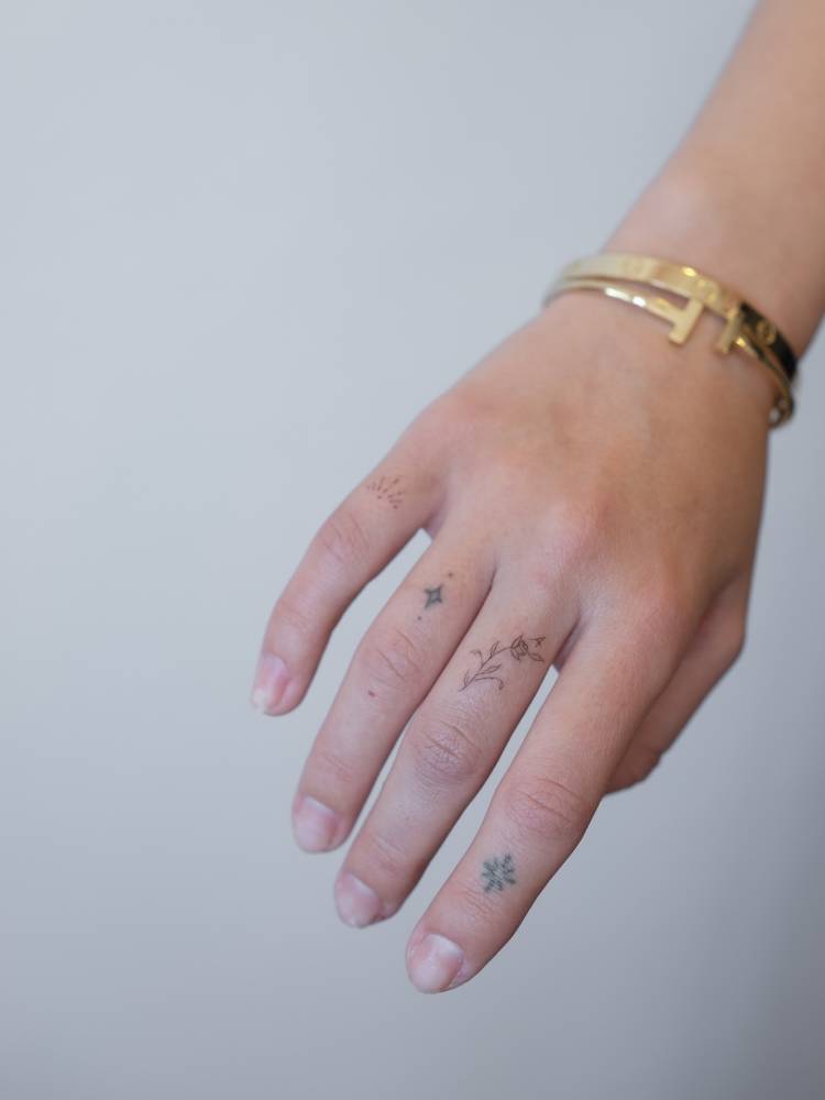 Tiny flower and letter "A" tattoo in fine line style located on the finger.