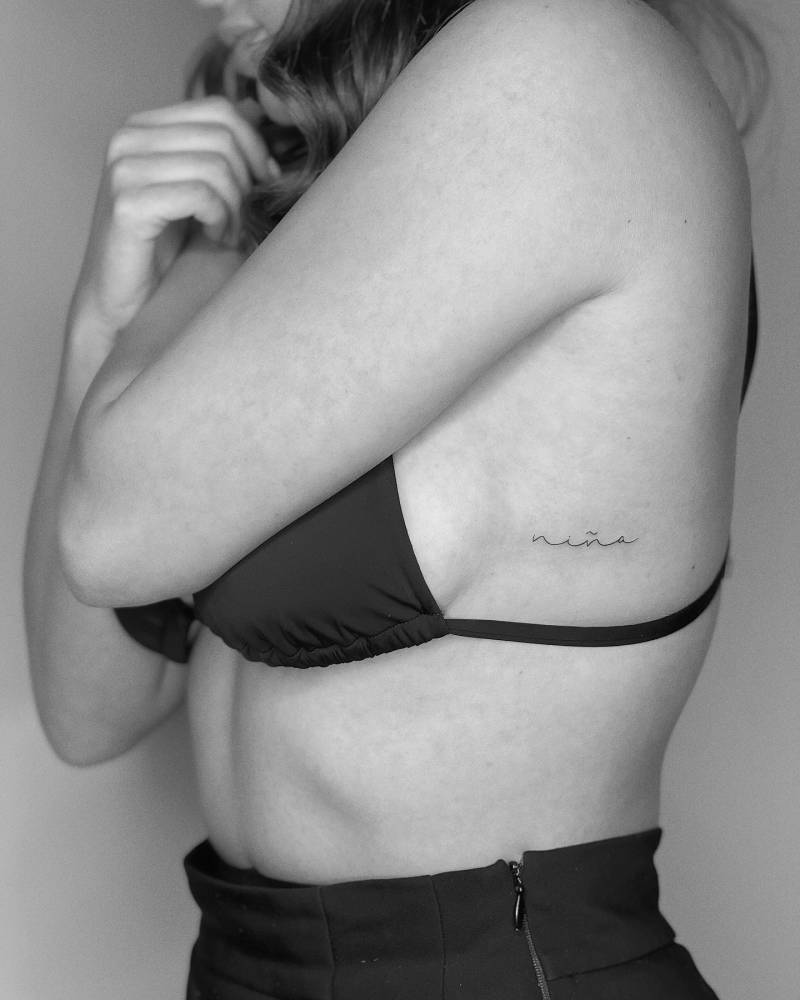 "Niña" handwritten lettering tattoo done on the side boob.