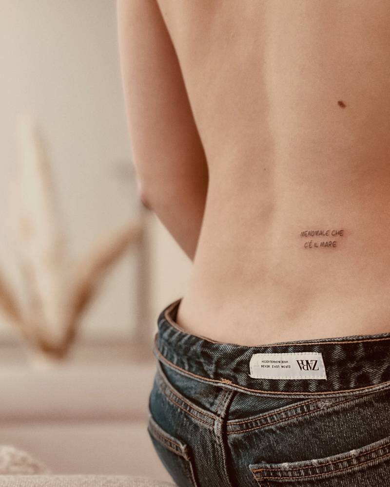 "Menomale che c'è il mare" lettering tattoo handwritten on the lower back.