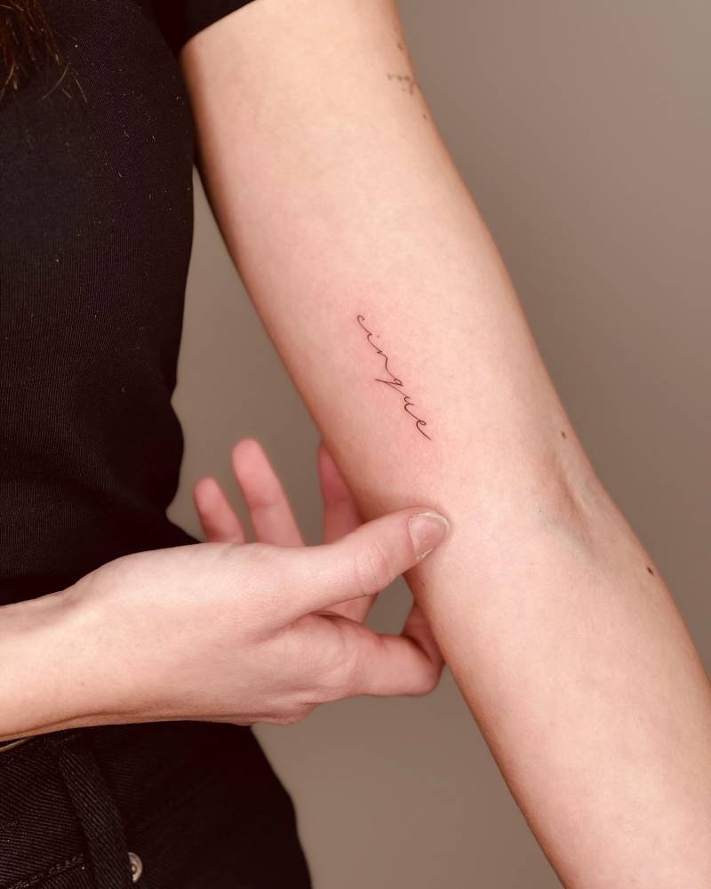 "Cinque" lettering tattoo in handwritten font located on the inner arm.